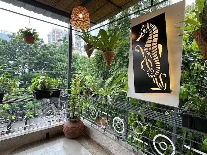 A balcony with hanging plants, a lit seahorse panel and trees outside