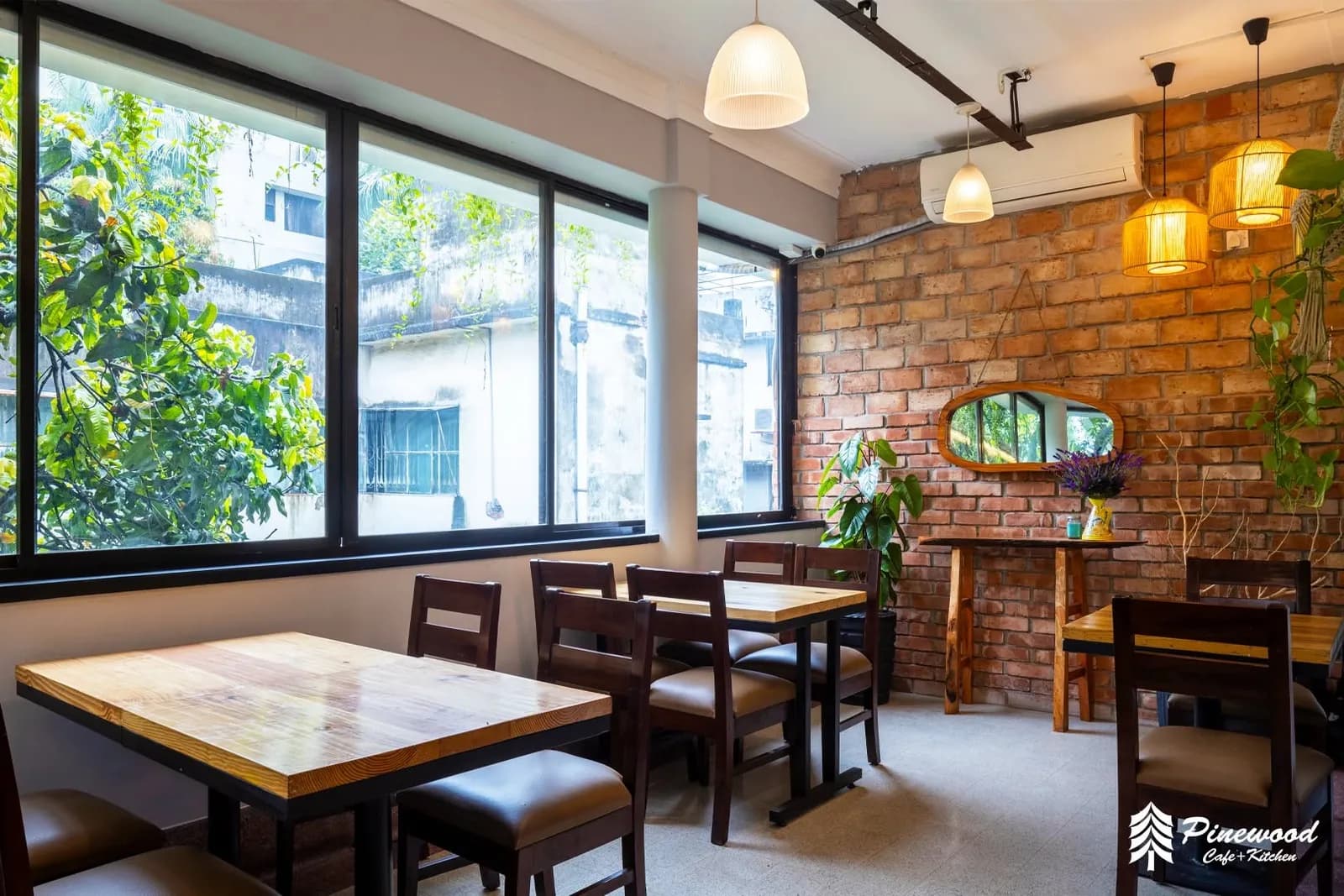 Wooden tables beside large windows and an exposed brick wall with a mirror