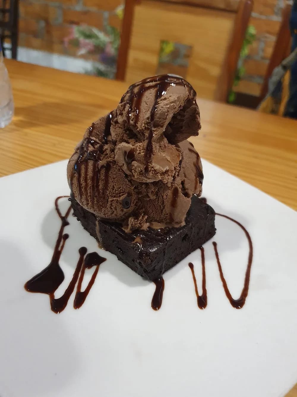A brownie with chocolate ice cream and chocolate sauce on a white plate