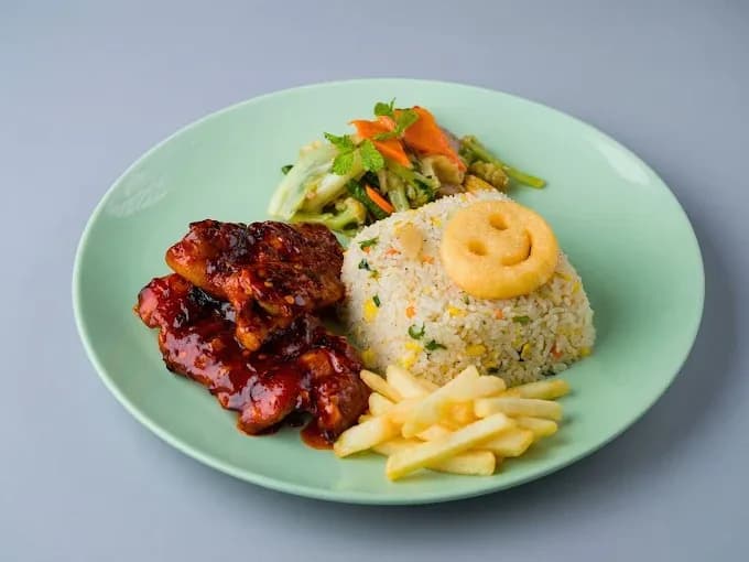 Glazed chicken with fried rice, vegetables and fries on a green plate