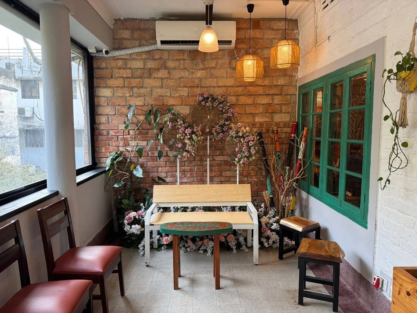 A corner with a brick wall, pink flower stands, a wooden bench, green windows and hanging lamps