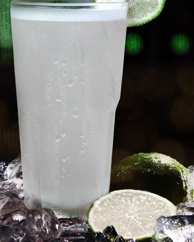 A tall glass of cold lemonade with a lime slice, on crushed ice