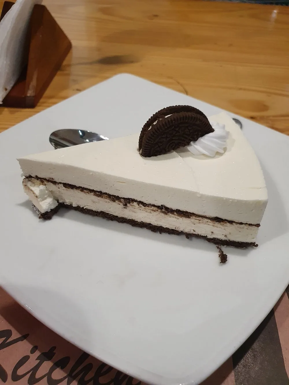 A slice of Oreo cheesecake with an Oreo and cream on top