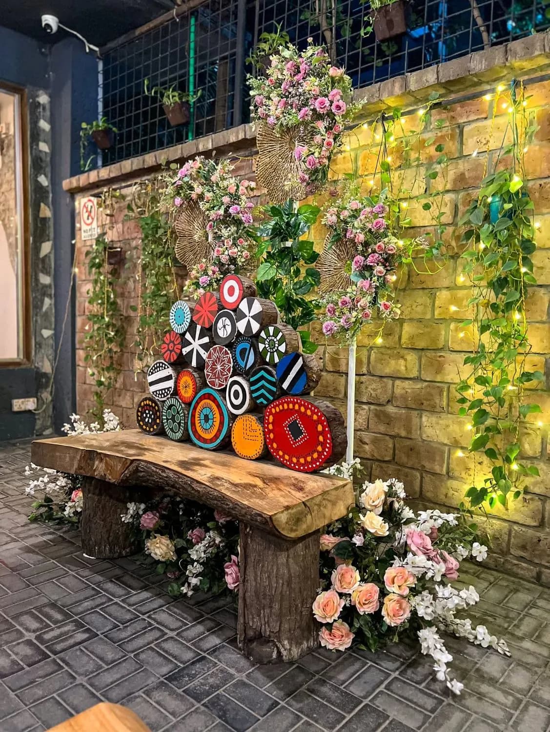 Wooden bench with painted log ends, flowers and fairy lights on a brick wall