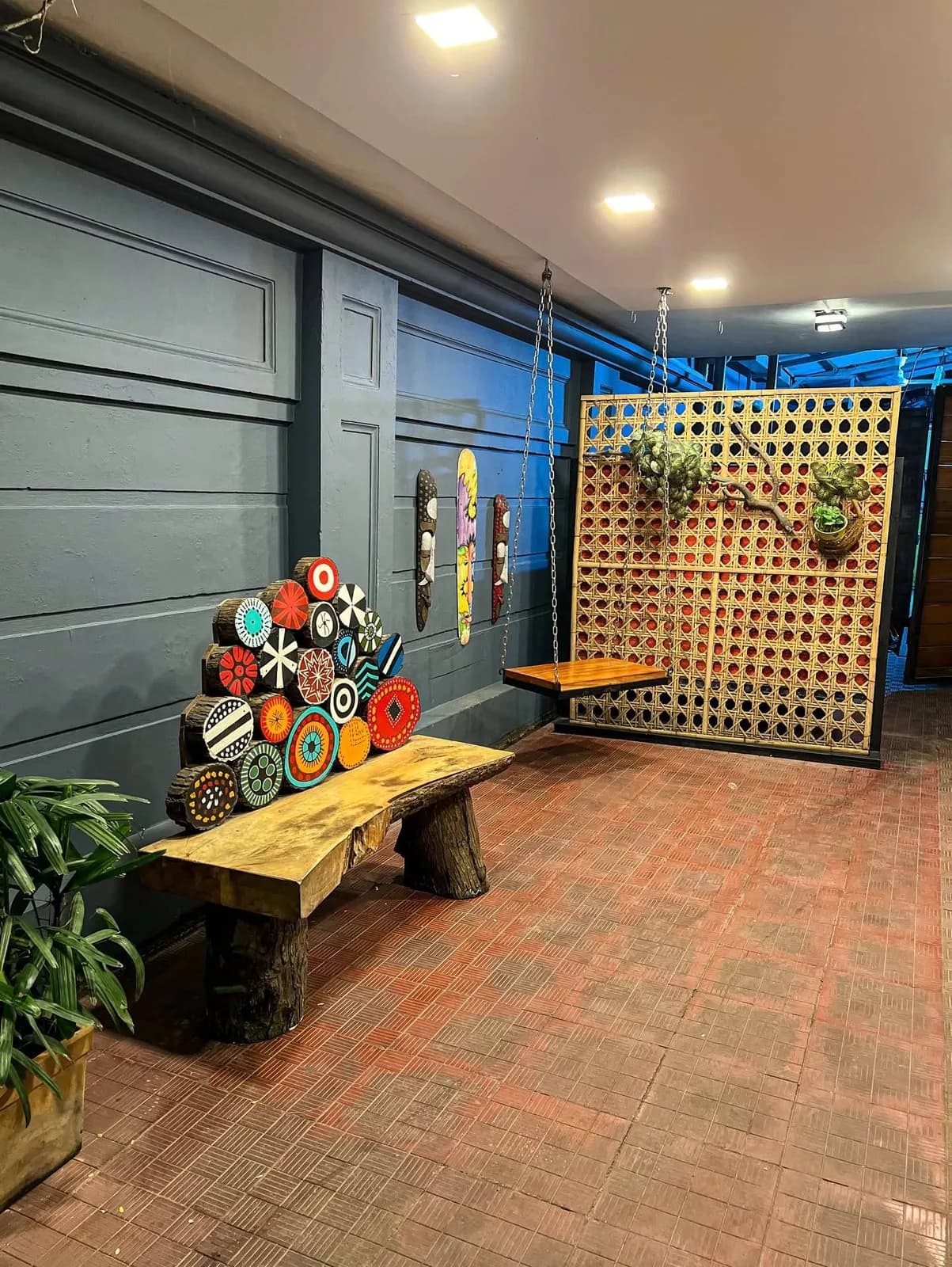 A wooden swing in front of a cane lattice screen, next to a painted log bench