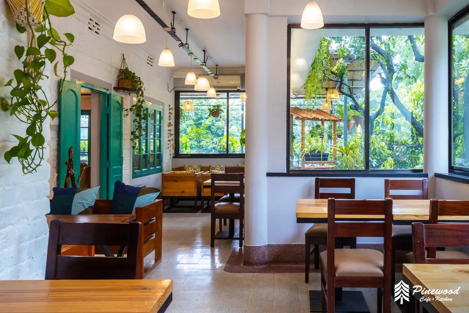Dining room with green doors, hanging plants and large windows onto trees